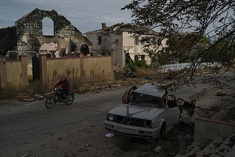 A man drives his motorcycle past a destroyed car in the retaken village of Velyka Oleksandrivka, Ukraine. (Photo | AP)