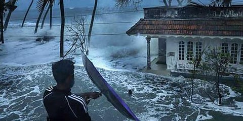 A man attempts to open an umbrella during a stormy weather as sea water enters Chellanam area following heavy rainfall in Kochi. (File Photo | PTI)