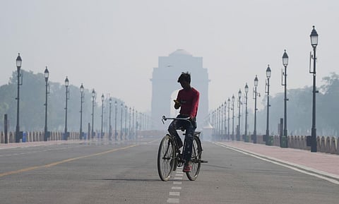 A man rides a bicycle down the Kartavya Path in the backdrop of India Gate, engulfed in smog, in New Delhi, October 24, 2022. (Photo | PTI)