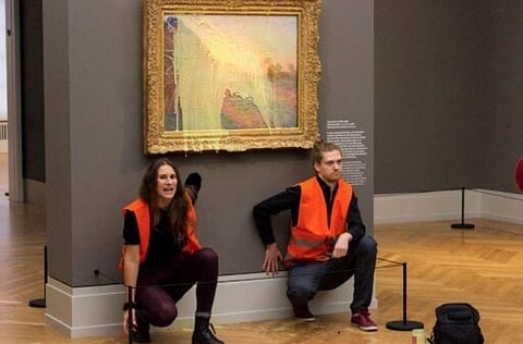 'Last Generation' shows activists of the group being glued underneath the painting 'Les Meules' after pouring mashed potatoes on the artwork in the Barberini museum. (Photo | AFP)