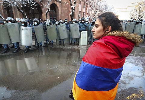 A woman wearing a state Armenian flag stands in front of a riot police line during a rally. (Photo | AP)