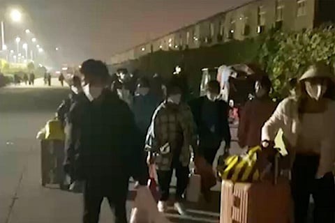 In this photo taken from video footage and released by Hangpai Xingyang, people with suitcases and bags are seen leaving from a Foxconn compound in Zhengzhou (Photo | AP)