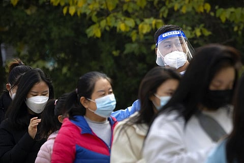 A worker wearing a face shield talks to people as they stand in line for COVID-19 tests at a coronavirus testing site in Beijing, Thursday, Nov. 10, 2022. (Photo | AP)