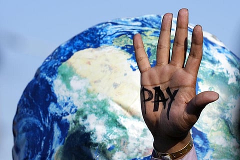 A hand reads 'pay' calling for reparations for loss and damage at the COP27 U.N. Climate Summit in Egypt, Nov. 18, 2022. (Photo | AP)
