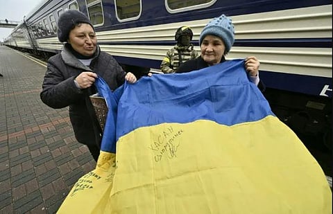 Local residents hold a Ukrainian flag on the station platform next to the first train from Kyiv to Kherson since the Russian invasion of Ukraine. (Photo | AFP)