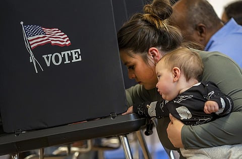 A woman hold her 11-month-old son while marking her ballot at a polling center. (Photo | AP)