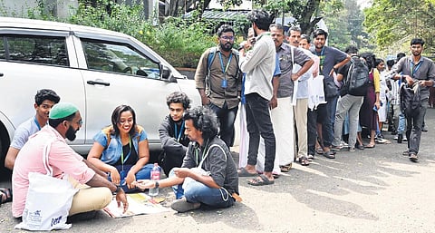 A group of youngsters brave the scorching sun as they sit to play traditional stone game to kill time after a long queue. (Photo | Vincent Pulickal, EPS)