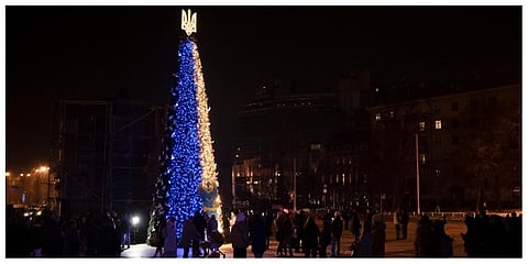 People gather around a Christmas tree decorated with the colors of the Ukrainian national flag at Sophia square in Kyiv. (Photo |AP)