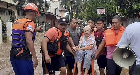 An elderly woman sits on a chair while being carried by coast guard personnel wading through floodwaters in Plaridel, Misamis Occidental province in the southern Philippines. (Photo | AP)