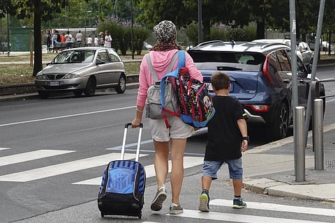Image used for representational purpose only. A woman carries backpacks as her son walks after coming out of a primary school, in Milan, Italy,  Sept. 14, 2022. (Photo | AP)