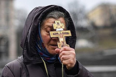 A religious woman holds a cross as she prays on Independence square in Kyiv in the morning of February 24, 2022. | AFP