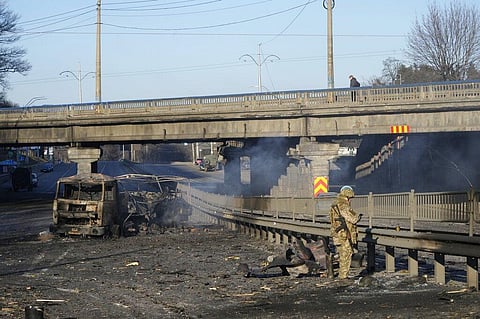A Ukrainian soldier investigates debris of a burnt military truck in a street in Kyiv, Ukraine, Saturday, Feb. 26, 2022.