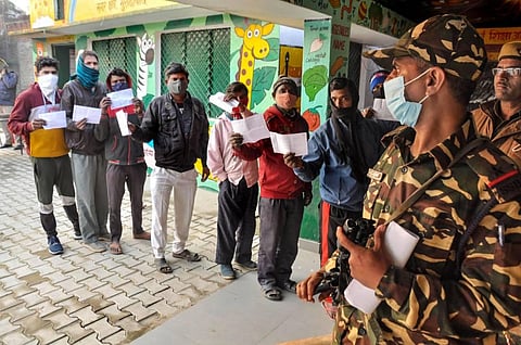 Security person stand guard as citizens wait to cast their vote at a polling booth. (Photo | PTI)