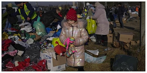 A Ukrainian refugee girl collects a toy from a pile of donated clothes at the Medyka border crossing, in Medyka, Poland. (Photo: AP)