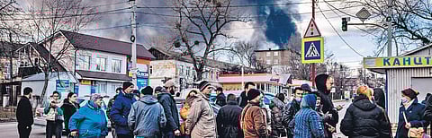 People stand in line in front of a supermarket, while smoke billows over the town of Vasylkiv just outside Kyiv on Sunday, after Russian strikes hit an oil depot (Photo | PTI)
