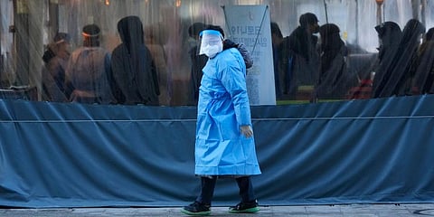 A medical worker passes by people as they wait for their coronavirus tests at a makeshift testing site in Seoul, South Korea. (Photo | AP)
