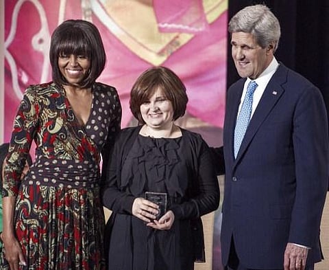 In this file photo taken on March 9, 2013 US First Lady Michelle Obama (L) and US Secretary of State John Kerry (R) stand for a photos with Elena Milashina (C) of Russia. (Photo | AFP)