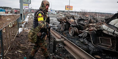 An armed man stands by the remains of a Russian military vehicle in Bucha, close to the capital Kyiv, Ukraine. (Photo | AP)