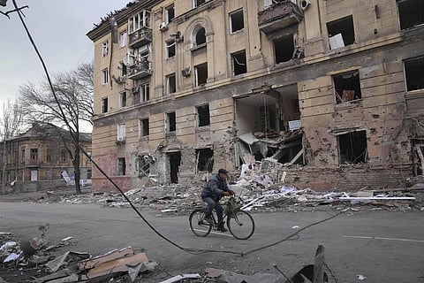 A man rides a bicycle in front of an apartment building that was damaged by shelling in Mariupol, Ukraine.  (Photo | AP)