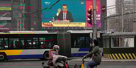 People ride past a large video screen at an intersection showing Chinese Premier Li Keqiang (Photo | AP)