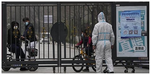 Residents in a locked down community look out from a closed gate as a worker in protective gear monitors access on Sunday, March 13, 2022, in Beijing. (Photo | AP)