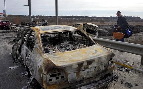 A resident passes by cars burnt in the Russian shellfire as he flees from his hometown on the road towards Kyiv, in the town of Irpin. (Photo | AP)