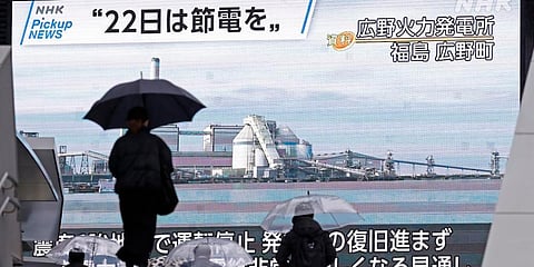 People walk by a huge monitor airing a news program which calls for power saving, in Tokyo. (Photo| AP)