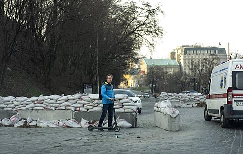 A man riding an electric scooter waits for traffic to stop as he makes his way through barricades in Kyiv, Ukraine. (Photo | AP)