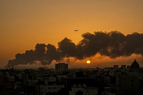 A passenger airplane flies over a smoldering fire at a Saudi Aramco oil depot after a Yemen Houthi rebel attack, ahead of a Formula One race as the sun rises in Jiddah, Saudi Arabia. (Photo | AP)