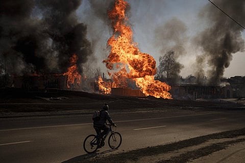 A man rides his bike past flames and smoke rising from a fire following a Russian attack in Kharkiv, Ukraine. (Photo | AP)
