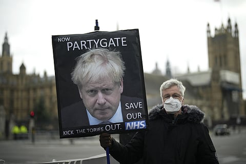 An anti-Conservative Party protester holds a placard with an image of British Prime Minister Boris Johnson including the words 'Now Partygate' backdropped by the Houses of Parliament, in London. (AP)