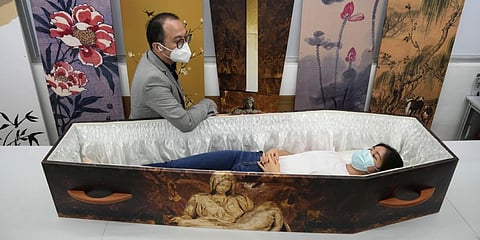 Wilson Tong, CEO of LifeArt Asia, left, talks to a reporter who tries out a catholic-designed paper coffin at Tong's factory in Hong Kong, Friday, March 18, 2022. (Photo | AP)