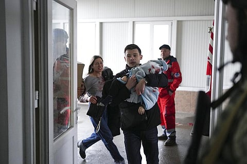 Marina Yatsko, left, runs behind her boyfriend Fedor carrying her 18 month-old son Kirill who was killed in shelling, as they arrive at a hospital in Mariupol. (Photo | AP)