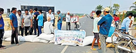 Farmers block the road by placing paddy bags at Tarasa in Rajkanika block. (Photo | EPS)