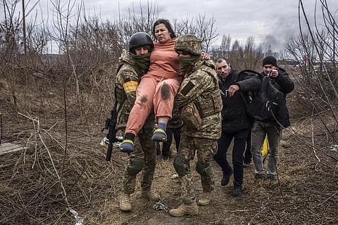A woman carried by Ukrainian soldiers crosses an improvised path while fleeing the town of Irpin, Ukraine. (Photo | AP)