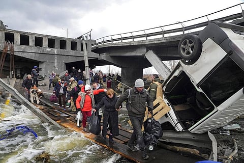People cross an improvised path under a destroyed bridge while fleeing the town of Irpin close to Kyiv, Ukraine. (Photo | AP)