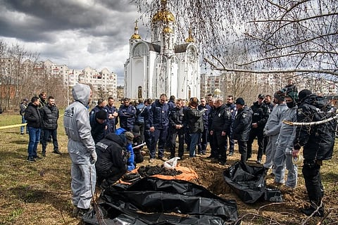 French forensics investigators, who arrived to Ukraine for the investigation of war crimes amid Russia's invasion, stand next to a mass grave in the town of Bucha. ( Photo | AP)