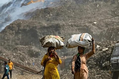 Ragpickers carrying sacks walk near New Delhi's Bhalaswa landfill, which has been on fire for three days. (Photo | AFP)