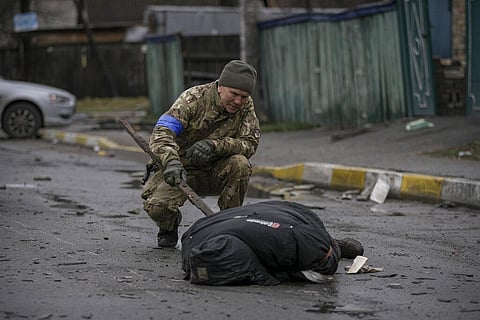 A Ukrainian serviceman uses a piece of wood to check if the body of a man dressed in civilian clothing is booby-trapped with explosive devices. (Photo | AP)