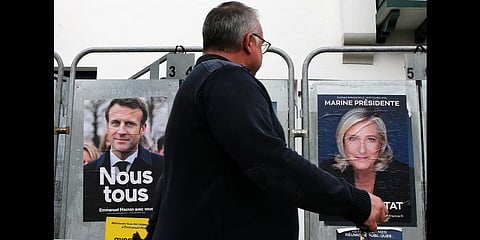A man walks past presidential campaign posters of french president Emmanuel Macron and centrist candidate for reelection and french far-right presidential candidate Marine Le Pen.(Photo | AP)