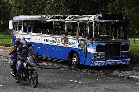 A Sri Lankan motorist rides past a burnt bus a day after clashes between government supporters and anti-government protesters in Colombo, Sri Lanka. (Photo | AP)