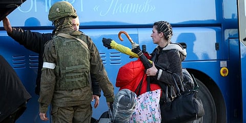 A woman leaves her shelter and walks to a bus escorted by a serviceman of Donetsk People's Republic militia in Mariupol. (Photo | AP)