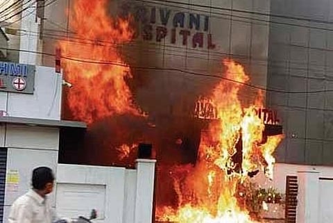 A commuter looks on as flames engulf a part of Srivani Hospital on Saturday . (Photo | EPS)