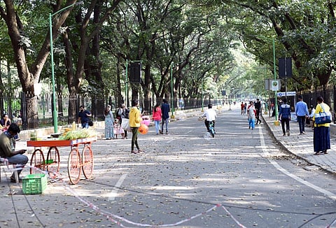 People take a walk at Cubbon park in Bengaluru as a hawker sells corn. (Photo | Nagaraja Gadekal, EPS)
