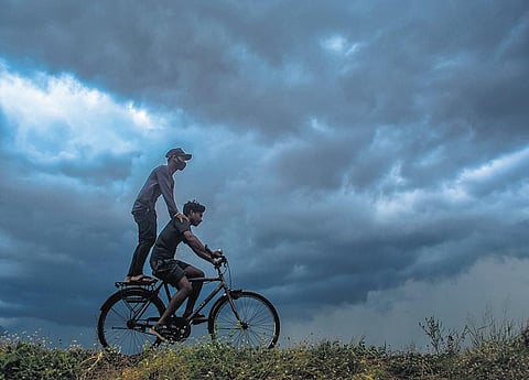 Boys ride a bicycle as dark clouds hover over the skyline of Bhubaneswar on Friday. (Photo | Express)