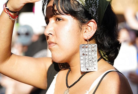 A woman wears earrings made out of birth control pills during a protest against the recent abortion law. (Photo | AP)