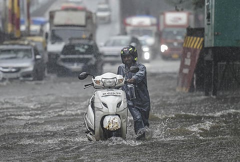 A man pushes his scooter through a flooded street following heavy monsoon rains, in Mumbai. (File Photo | PTI)
