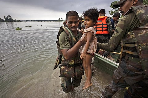 An Indian army soldier carries a girl to a safer place after she along with her family was rescued from flooded Tarabari village in Assam. (Photo | AP)
