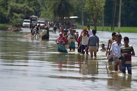 Villagers wade through a flooded road after heavy rainfall in Hojai district of Assam. (Photo | PTI)