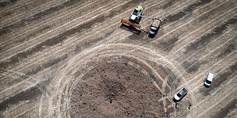 A farmer collects harvest on a field around a crater left by a Russian rocket ten kilometres from the front line in the Dnipropetrovsk region, Ukraine. (Photo | AP)